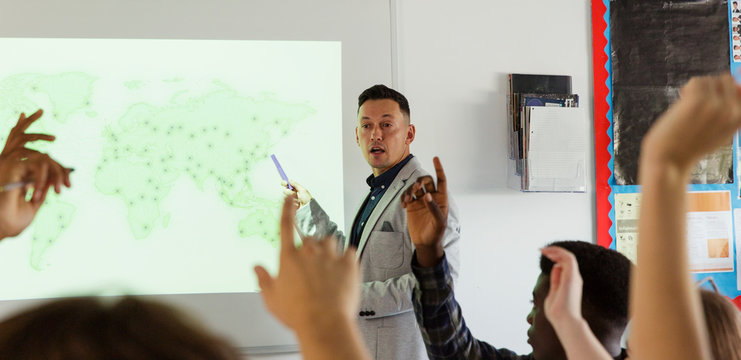 Male high school teacher leading lesson at projection screen in classroom