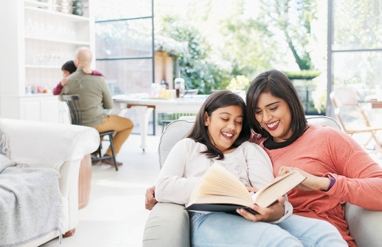 Mother and daughter reading book in living room