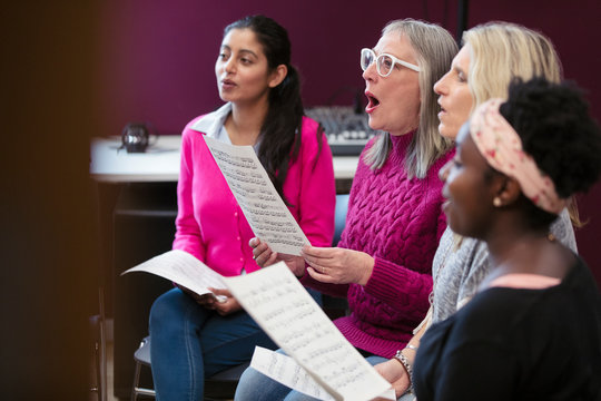 Womens choir with sheet music singing in music recording studio
