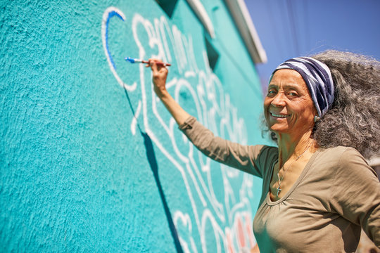 Portrait happy senior female volunteer painting on sunny wall