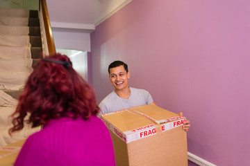 Happy couple moving into new house, carrying cardboard boxes up stairs