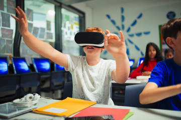 Curious junior high school boy student using virtual reality simulator in classroom