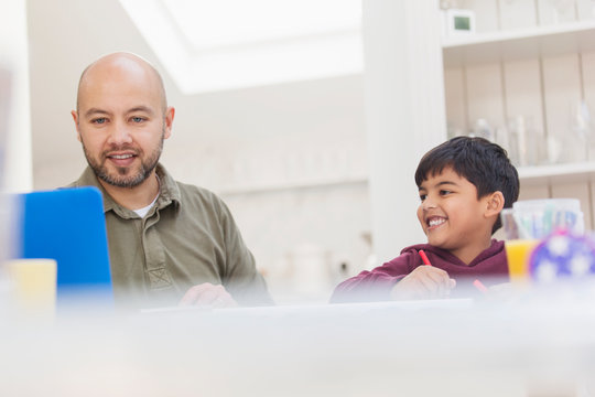 Father and son using laptop and coloring at table