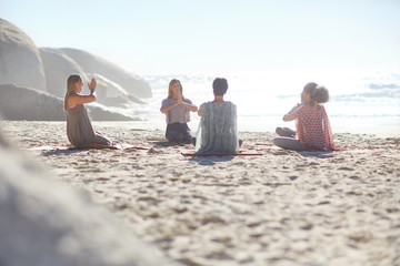 Group meditating in circle on sunny beach during yoga retreat