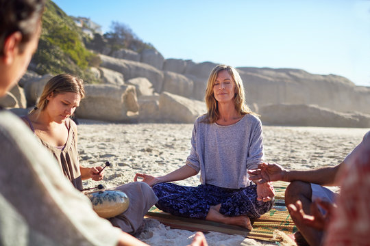 Serene woman meditating in circle on sunny beach during yoga retreat
