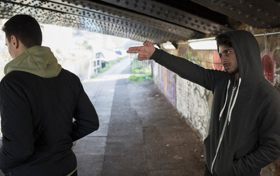 Menacing young man gesturing finger gun at man in urban tunnel