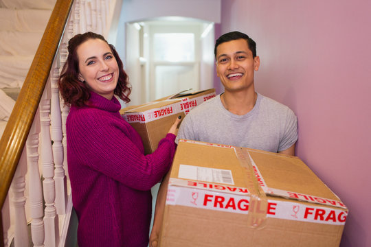 Portrait happy couple moving house, carrying cardboard boxes in corridor