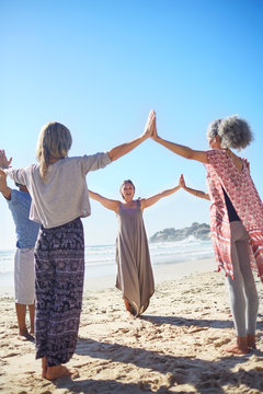 Group joining hands in circle on sunny beach during yoga retreat
