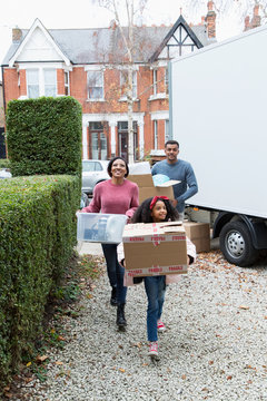 Family Moving Into New House, Carrying  Belongings From Moving Van In Driveway