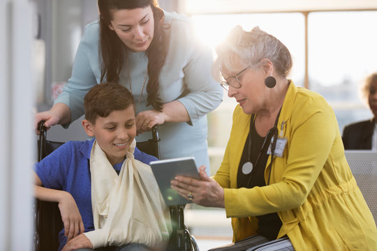 Doctor with digital tablet talking to boy patient in wheelchair and mother in clinic lobby