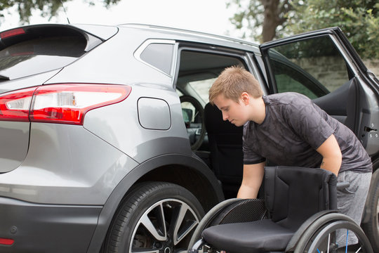 Young Woman Loading Wheelchair Into Back Seat Of Car