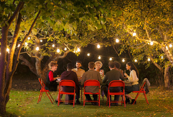 Friends enjoying dinner garden party under trees with fairy lights