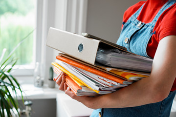 Young female college student carrying stack of books and binder