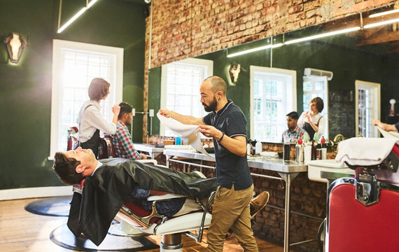 Male barber preparing to steam face of customer before shave in barbershop