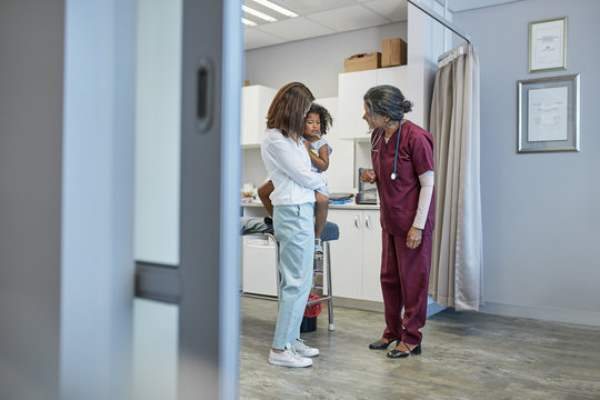 Female pediatrician talking mother daughter in clinic examination room