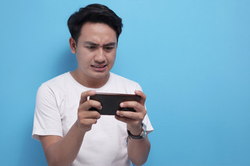 Funny Young Asian Guy Playing Games on Tablet Smart Phone