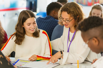 Female high school teacher helping girl student with homework in classroom
