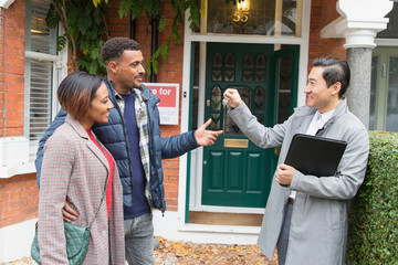 Real estate agent giving house keys to couple outside house for sale