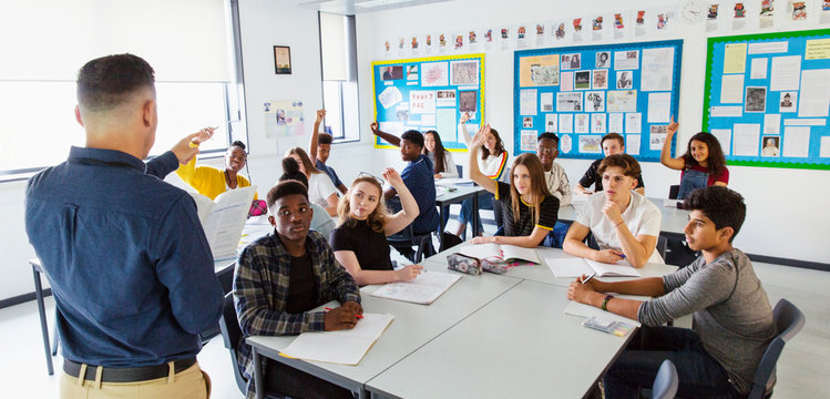 High School Teacher Calling On Students With Hands Raised In Classroom