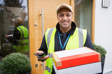 Portrait confident, friendly deliveryman with package and smart phone at front door