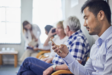 Man using smart phone, waiting in clinic waiting room