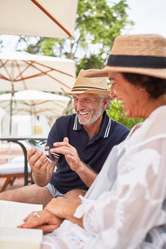 Happy Mature Couple Using Smart Phone At Resort Poolside