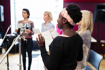 Womens choir with sheet music singing in music recording studio