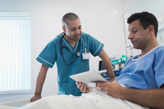 Male Nurse Talking With Patient Using Digital Tablet In Hospital Bed