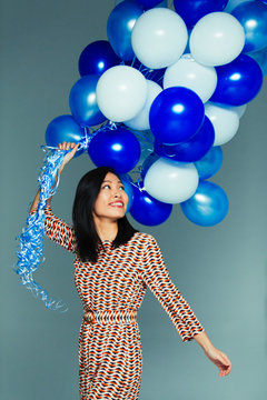 Smiling, carefree woman with blue and white balloon bunch