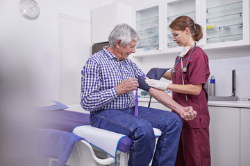 Female nurse checking blood pressure of senior male patient in clinic examination room