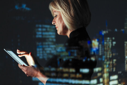 Double exposure businesswoman using digital tablet against highrise lights at night