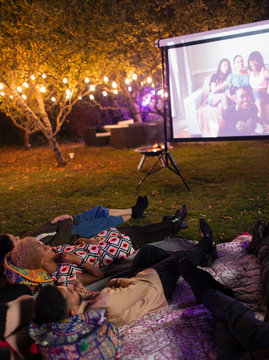 Friends relaxing, watching movie on projection screen in backyard