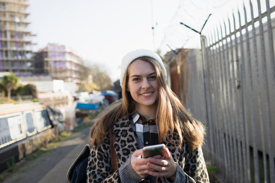 Portrait smiling young woman with smart phone on urban sidewalk