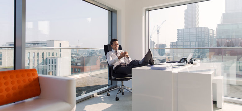 Businessman with feet up on desk in sunny, modern, urban office