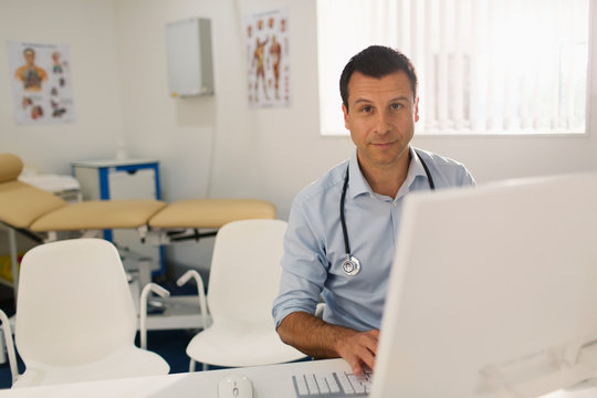 Portrait confident male doctor working at computer in doctors office