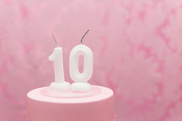 Birthday cake with candles as number ten on pink arabesques background.
