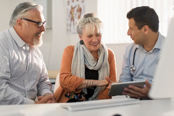 Doctor with digital tablet meeting with couple in doctors office