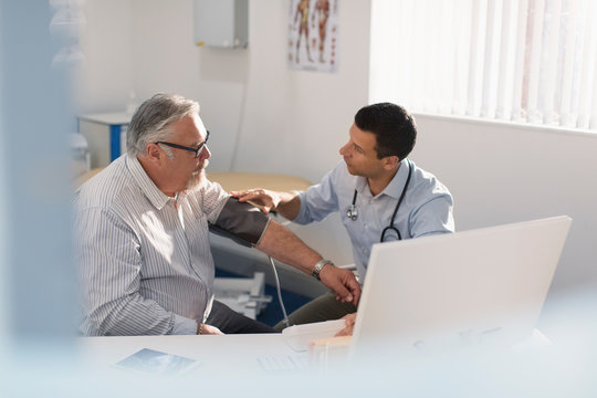 Male doctor checking blood pressure of senior patient in doctors office