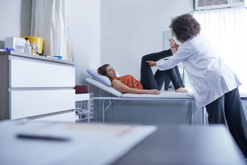 Female doctor examining leg of patient in clinic examination room