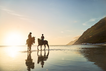 Young women horseback riding in tranquil ocean surf at sunset