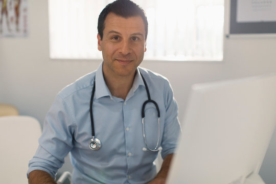 Portrait confident male doctor working at computer in doctors office