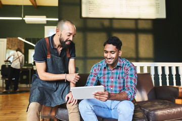 Male barber and customer using digital tablet in barbershop