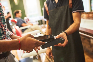 Male customer paying barber with smart phone contactless payment in barbershop