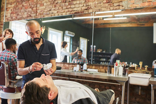 Male barber preparing to shave face of customer in barbershop