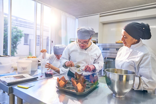 Chef helping student with Down Syndrome baking muffins in kitchen