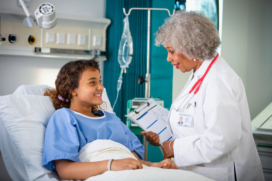 Female doctor talking with girl patient in hospital room