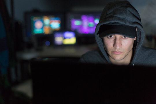 Male Hacker In Hoody Using Computer In Dark Room