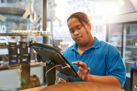 Young woman with Down Syndrome working at cash register in cafe