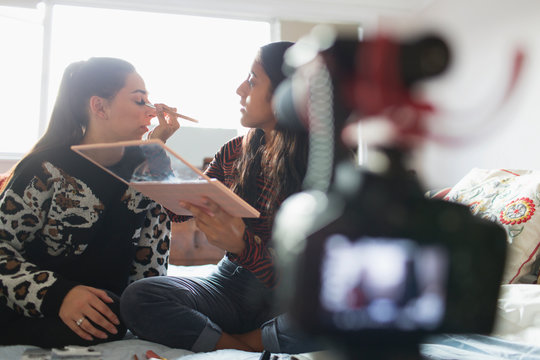 Teenage girls vlogging, demonstrating makeup application in bedroom