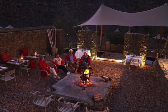 Senior Friends Relaxing With Wine At Fire Pit On Hotel Patio